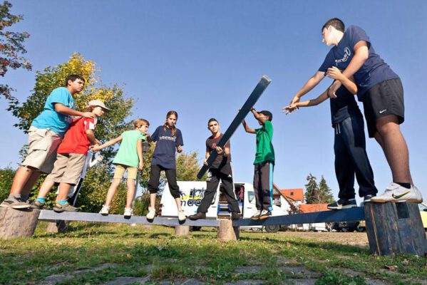 Kinder balancieren auf einem Balken im kooperativen Spiel